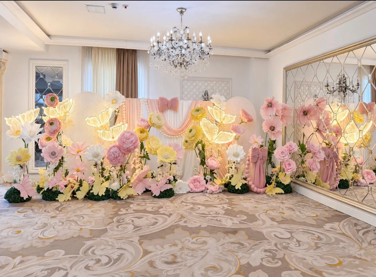 Sală de eveniment cu un perete de flori uriașe din hârtie și fluturi luminoși